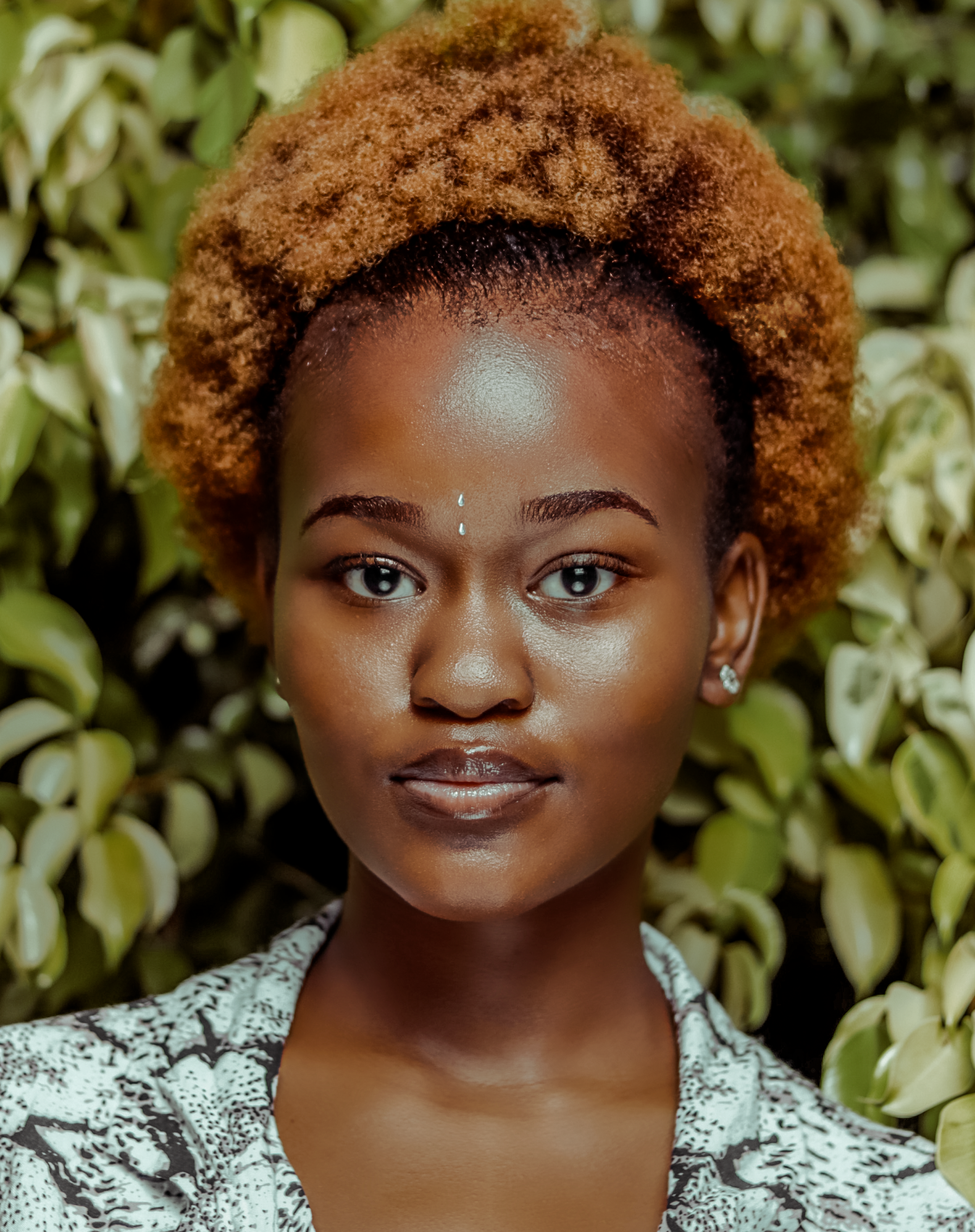 A close up of a woman 's face with a bush in the background.
