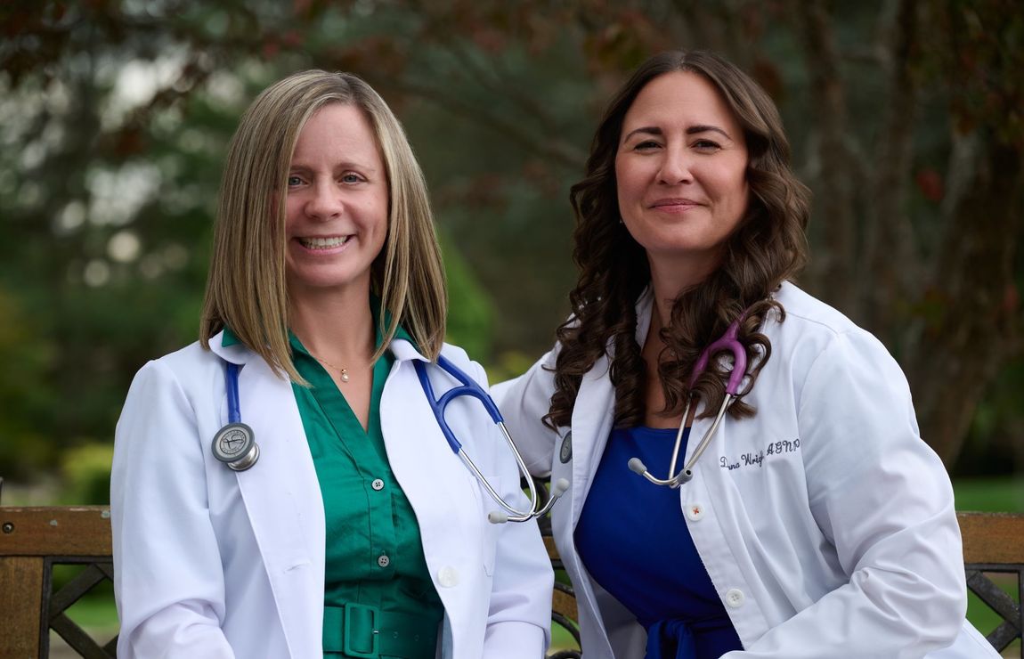 Two smiling doctors in white coats outdoors, seated together with stethoscopes visible.