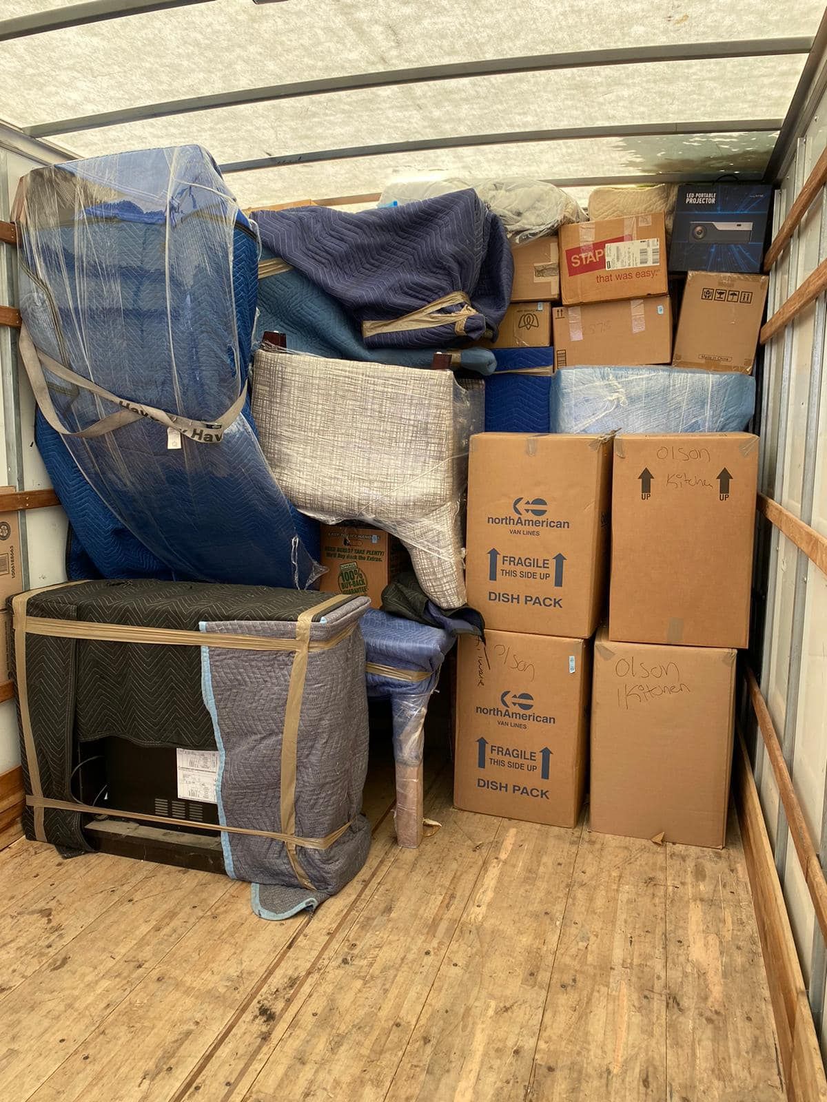 Inside a moving truck packed with furniture, boxes, and protective coverings.