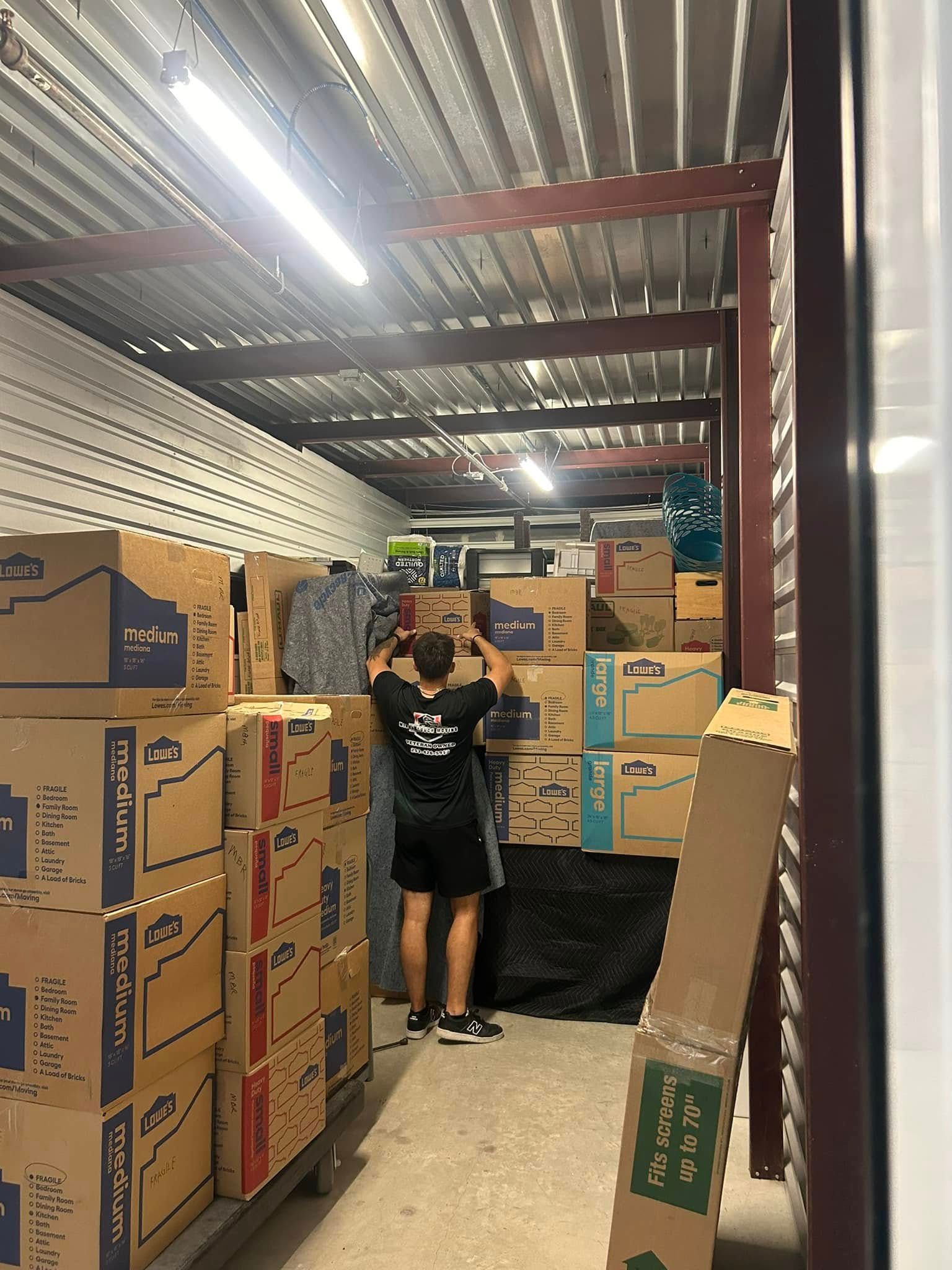 Person in storage unit stacking boxes with clothes and other items.