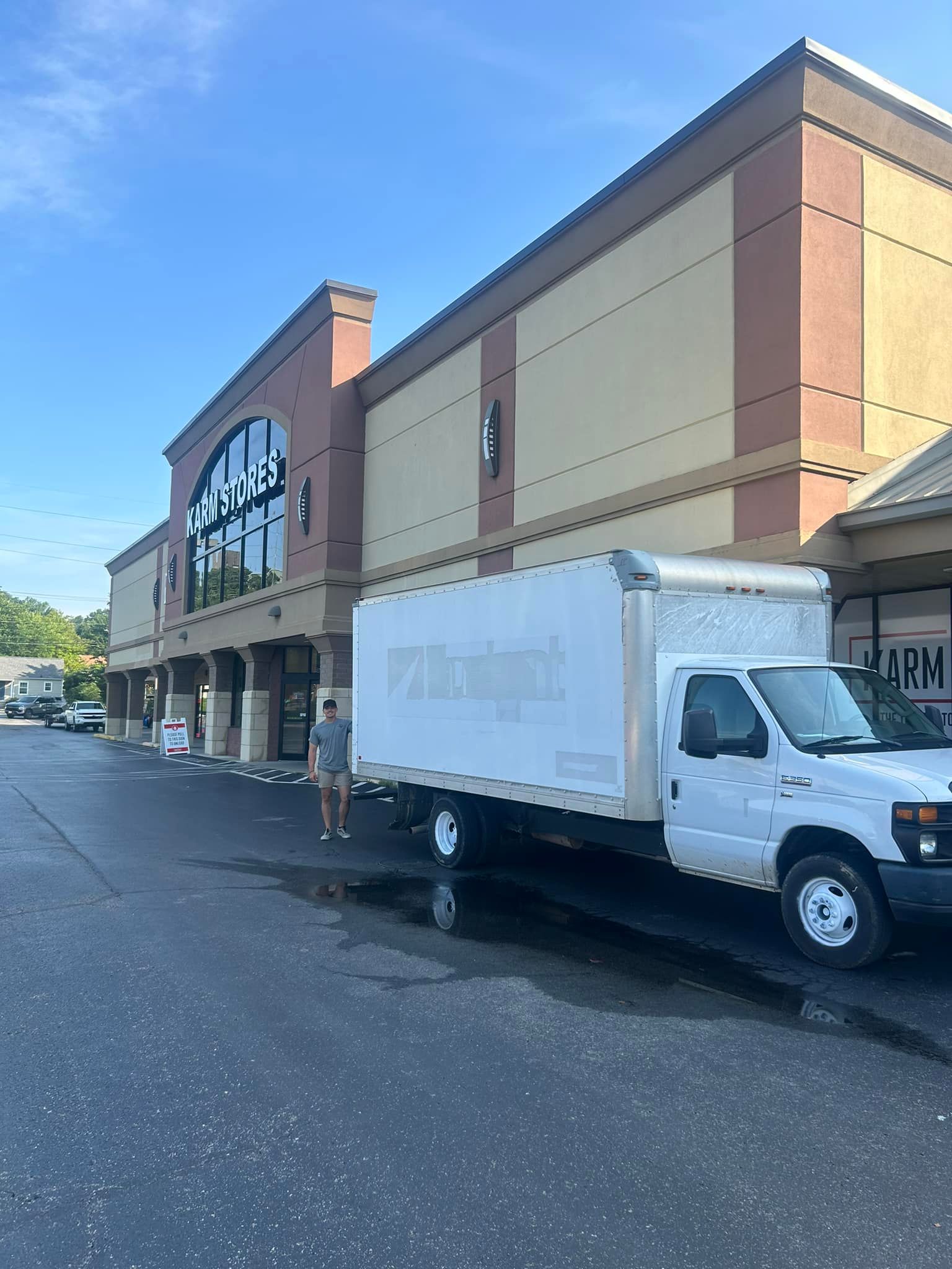 White delivery truck parked in front of a shopping center. A person stands nearby.