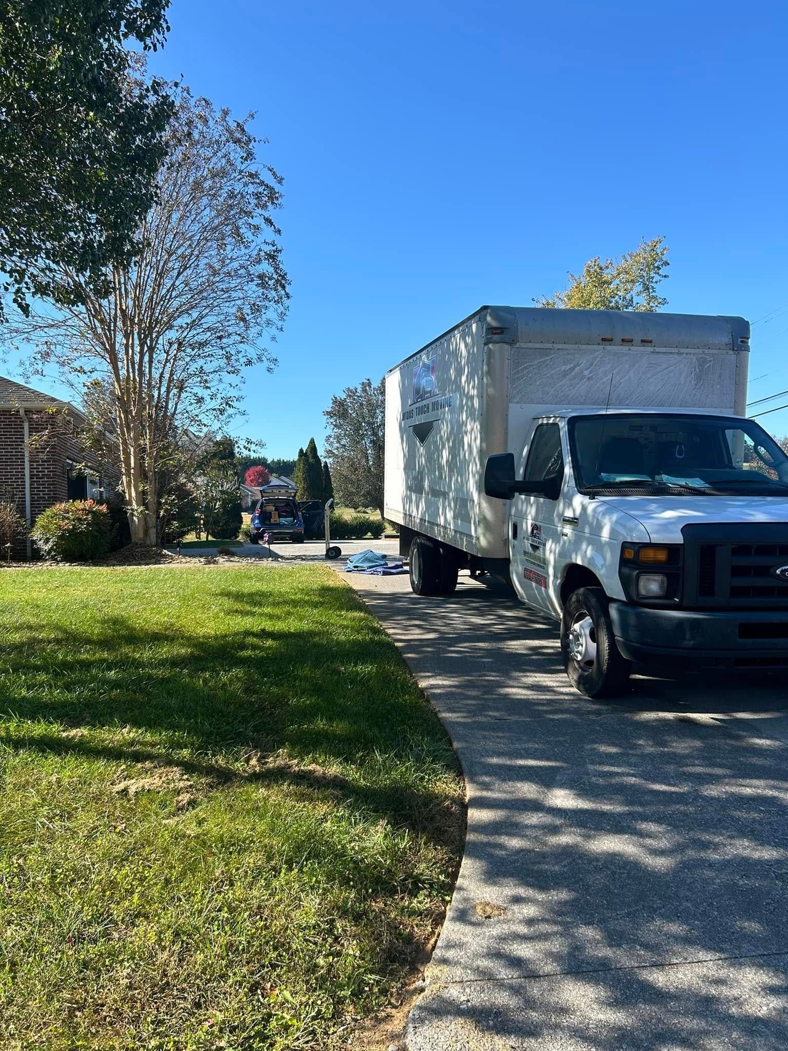 White moving truck parked on a driveway in front of a house on a sunny day.