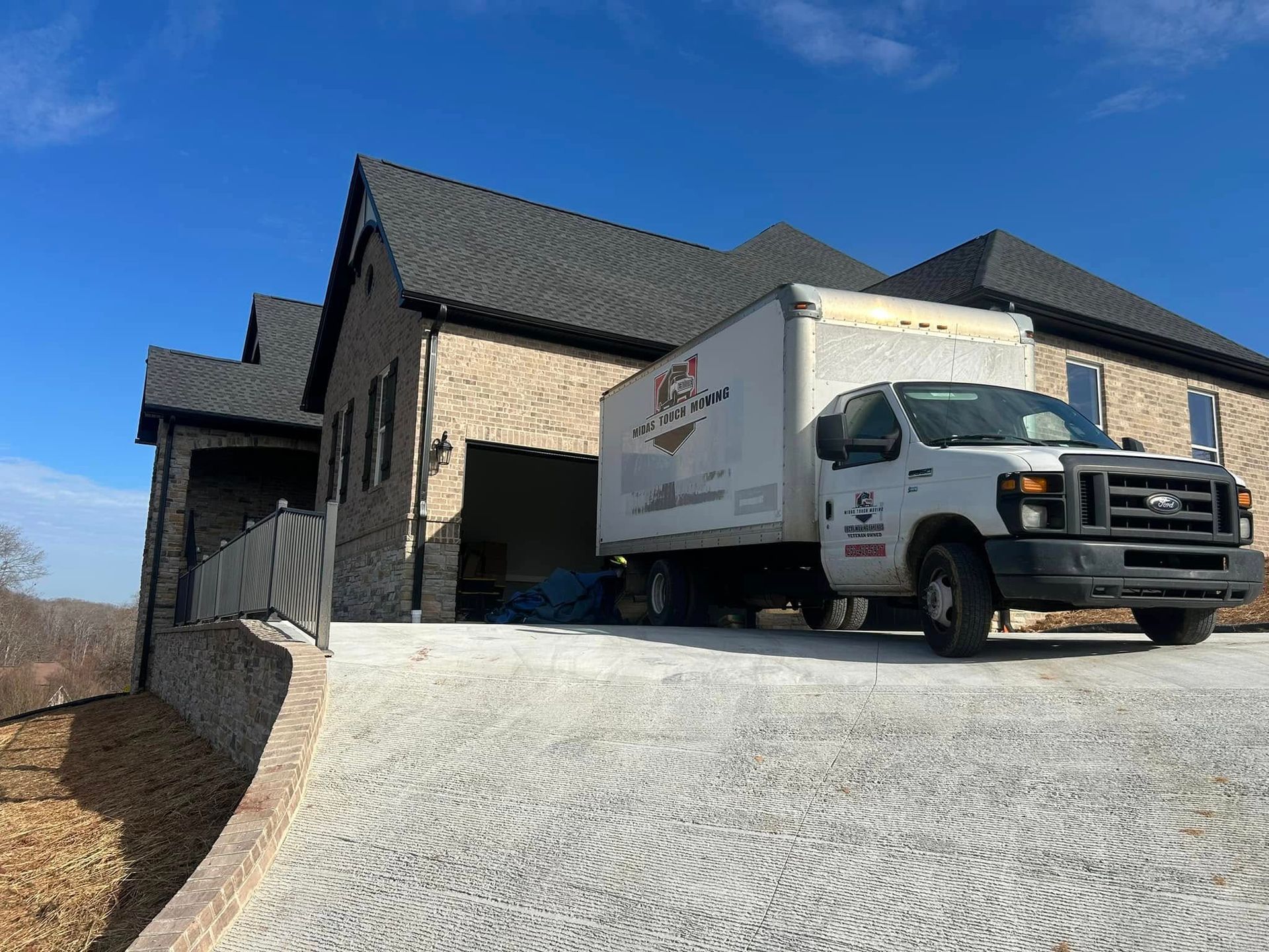 Moving truck parked in front of a stone house, unloading goods on a sunny day.