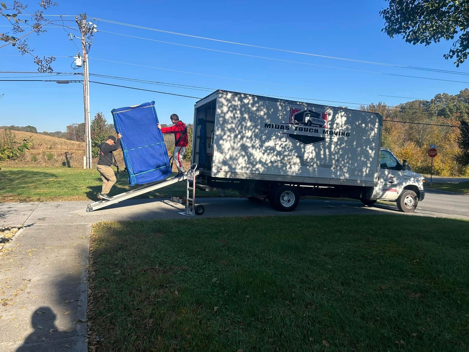Two movers loading a blue object onto a moving truck on a sunny day.