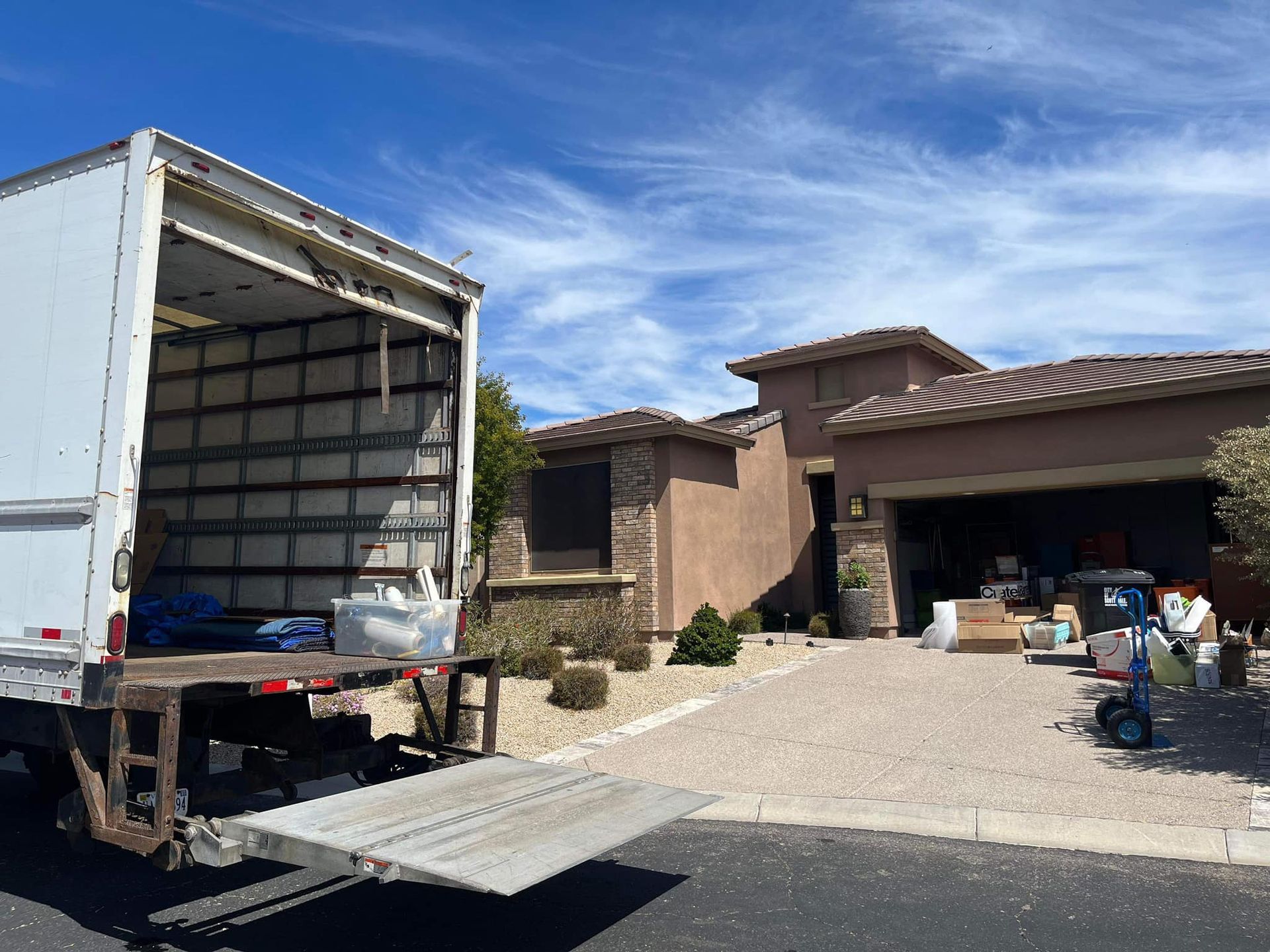 Moving truck parked in front of a house. Boxes and a dolly sit near the garage.