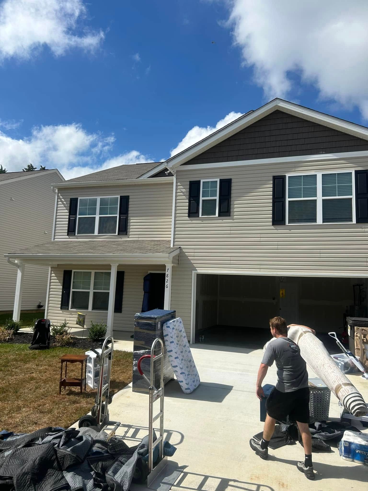 Moving day: Person loading a truck with furniture in front of a two-story beige house under a partly cloudy sky.