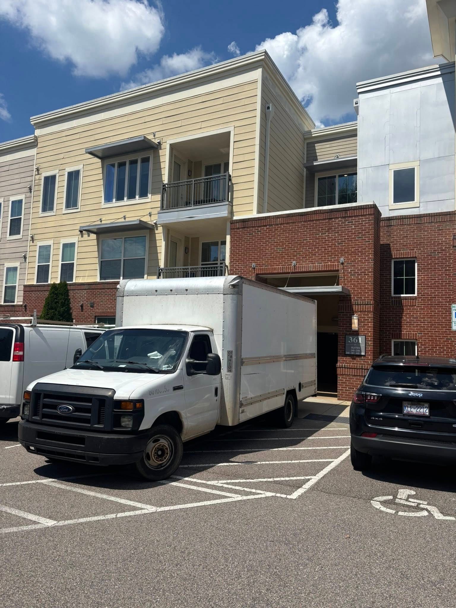 White moving van parked in front of a multi-story building. Sunny day.