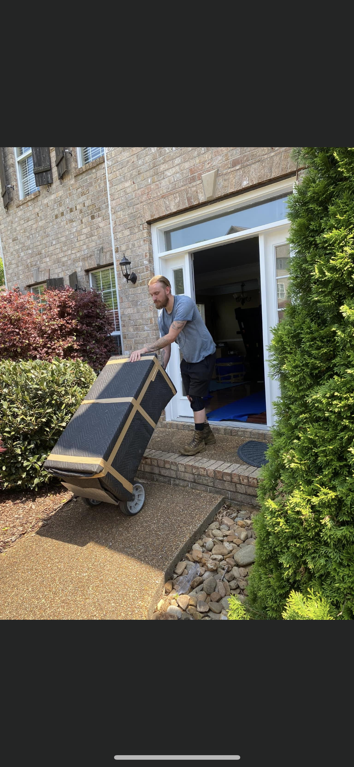 Man pulling a large, wheeled box towards an open doorway of a stone building.
