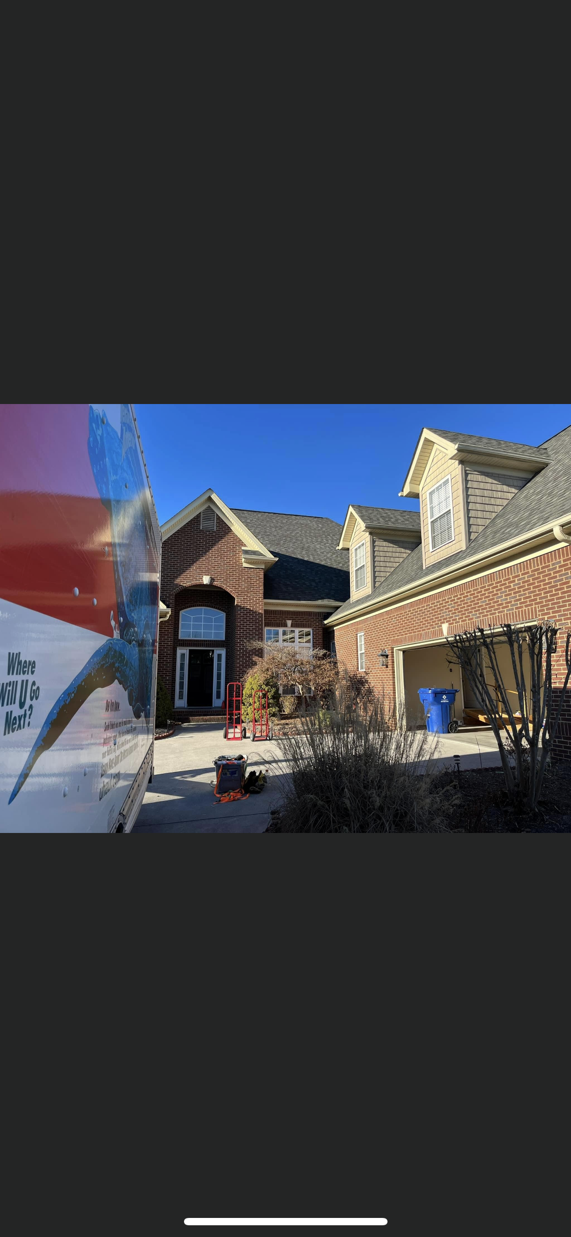 A house with a driveway and garage, a blue sky is above. A large truck is on the left.