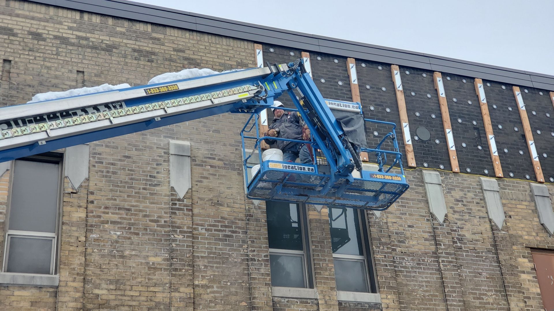 Un homme travaille sur une grue sur le côté d'un bâtiment.
