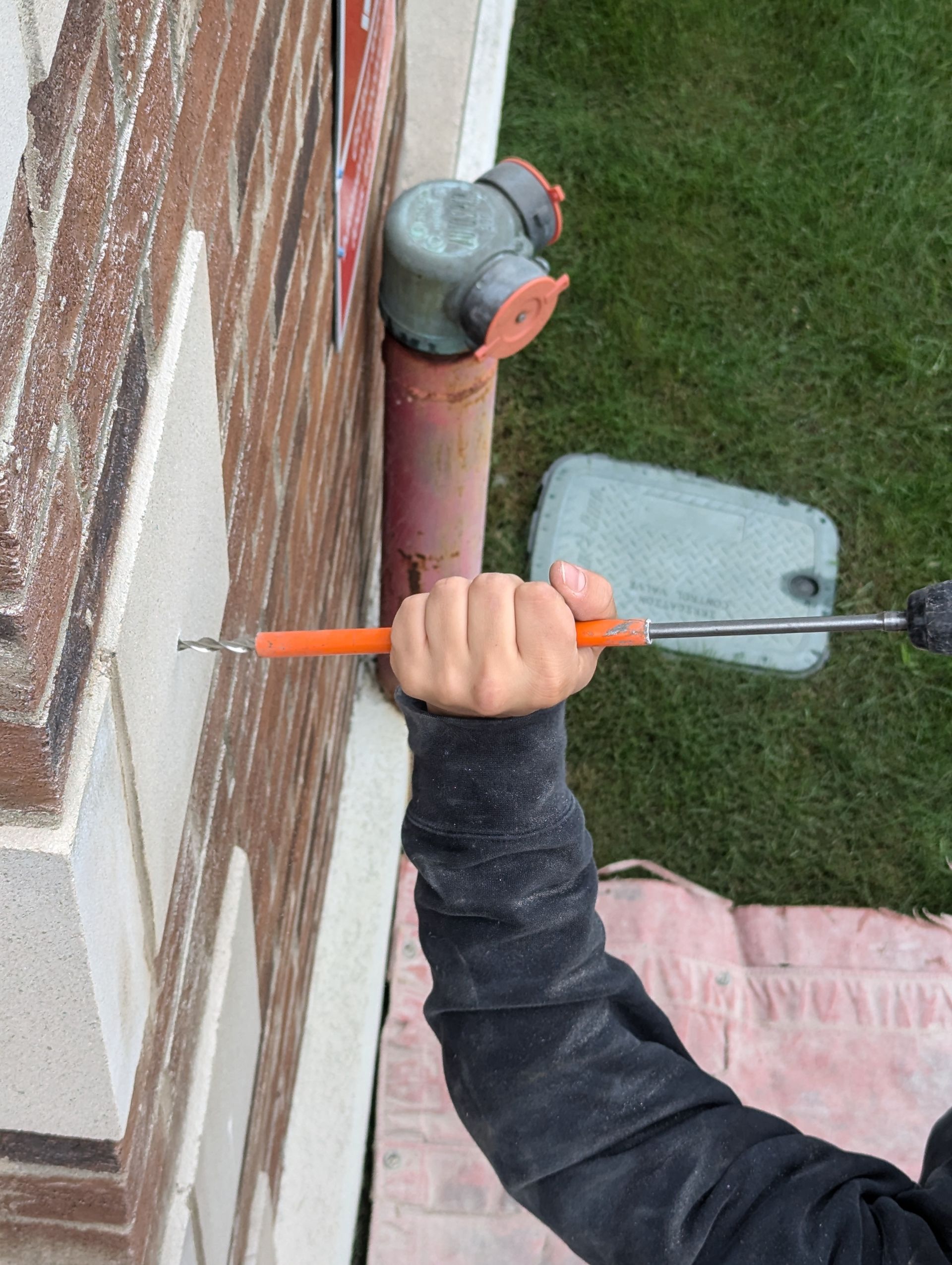 Une personne utilise un tournevis pour fixer un tuyau sur un mur de briques