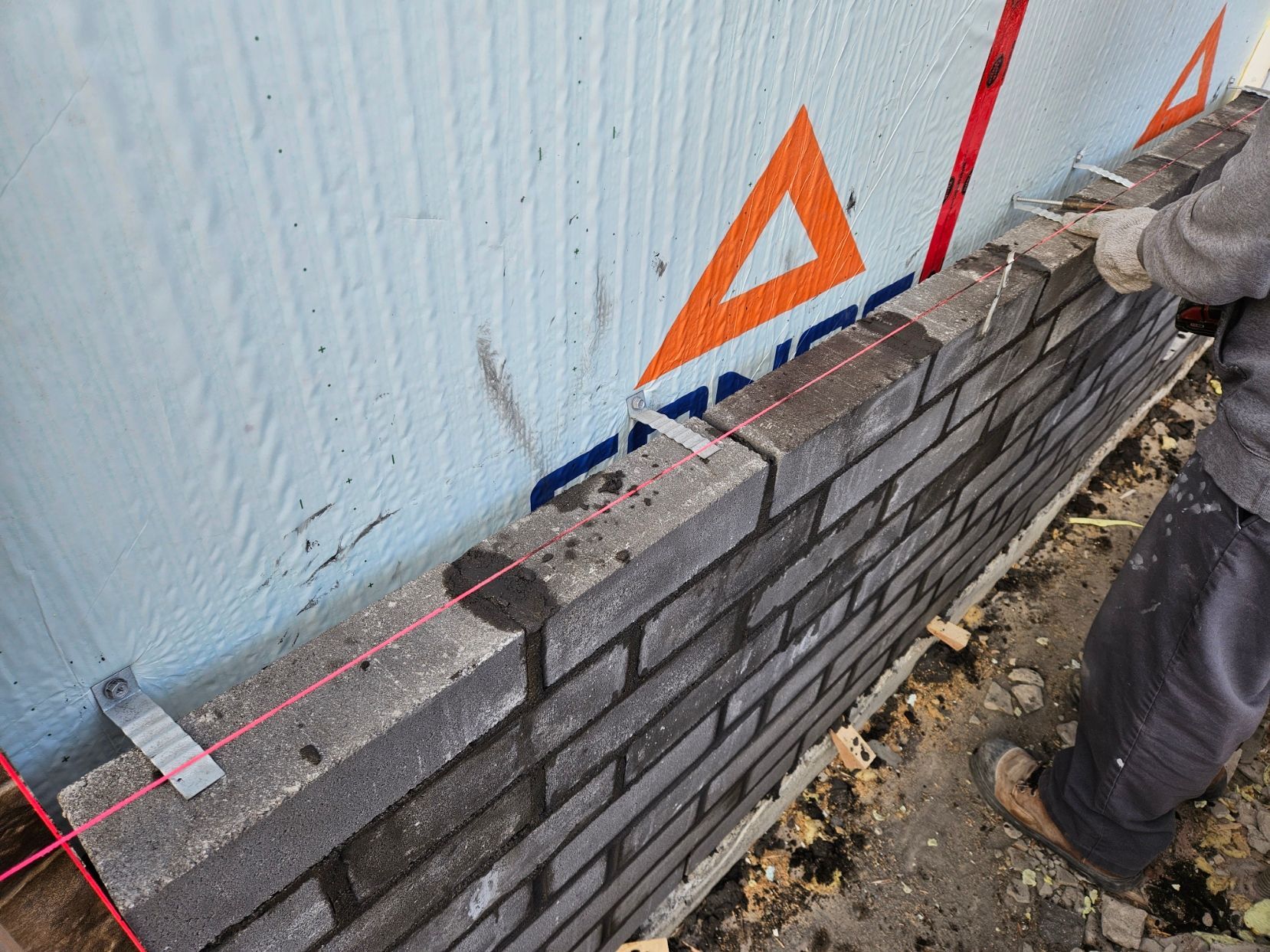 Un homme mesure un mur de briques avec un ruban à mesurer.