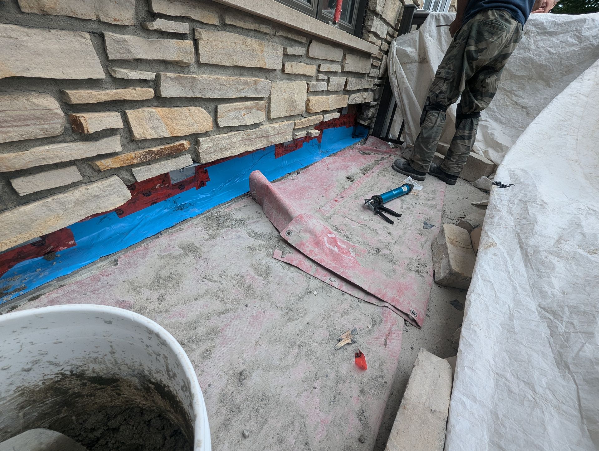 Un homme travaille sur un mur de pierre à côté d'un seau de ciment.