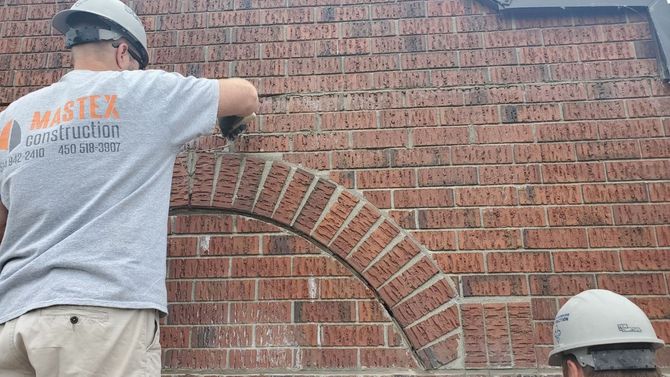 Un homme portant un casque travaille sur un mur de briques.