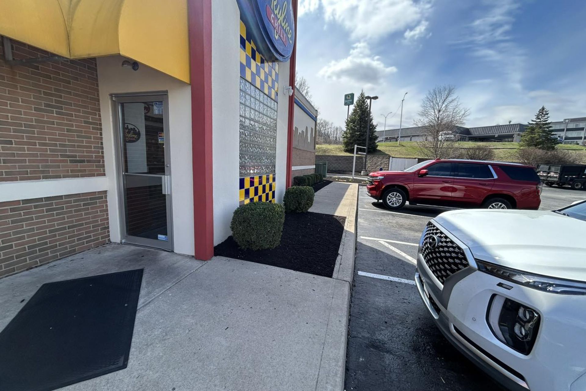 Exterior of a restaurant with a red SUV parked next to a white SUV on a sunny day.