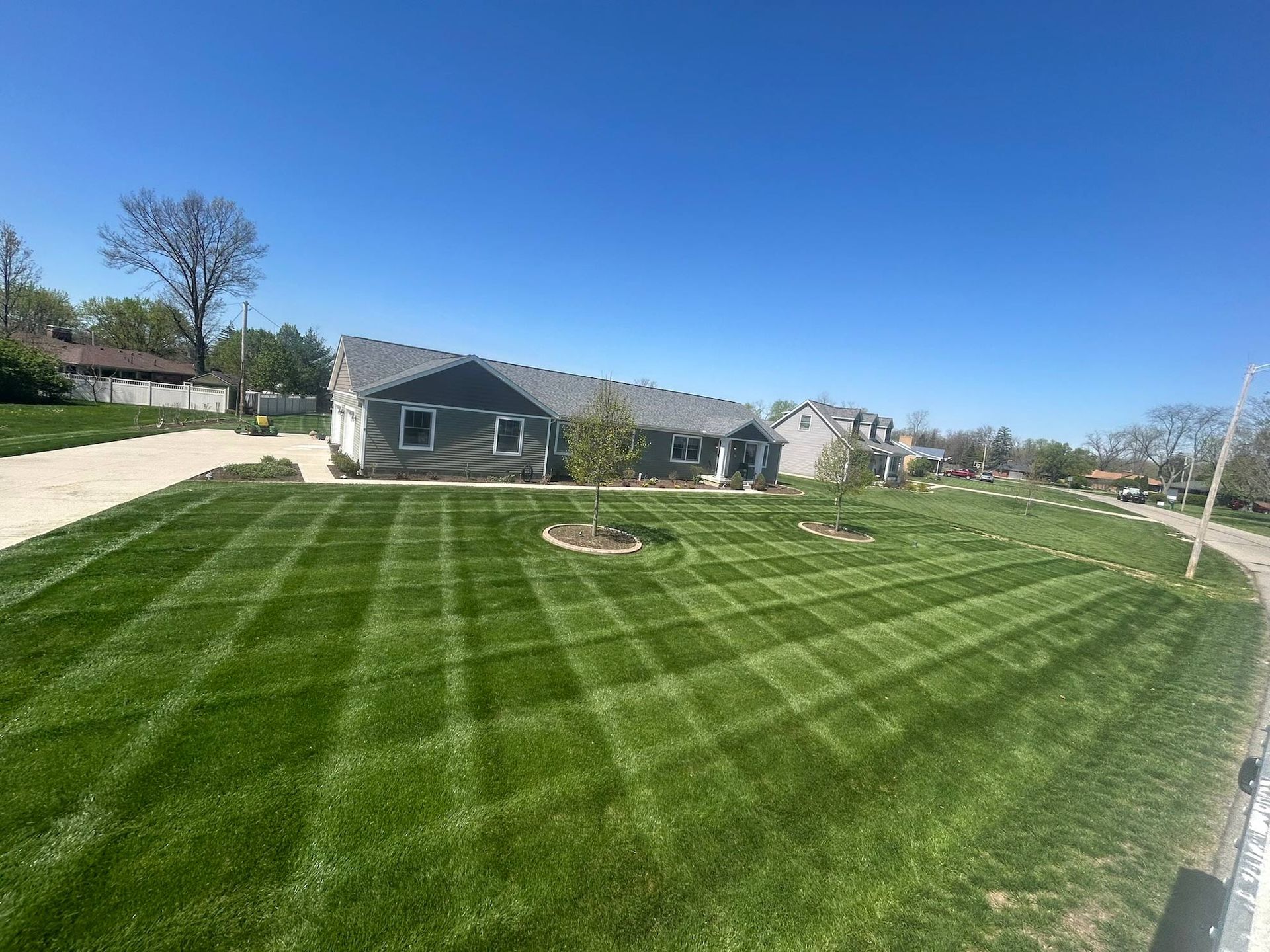 Lawn with checkered mowing pattern in front of a gray house under a clear blue sky.