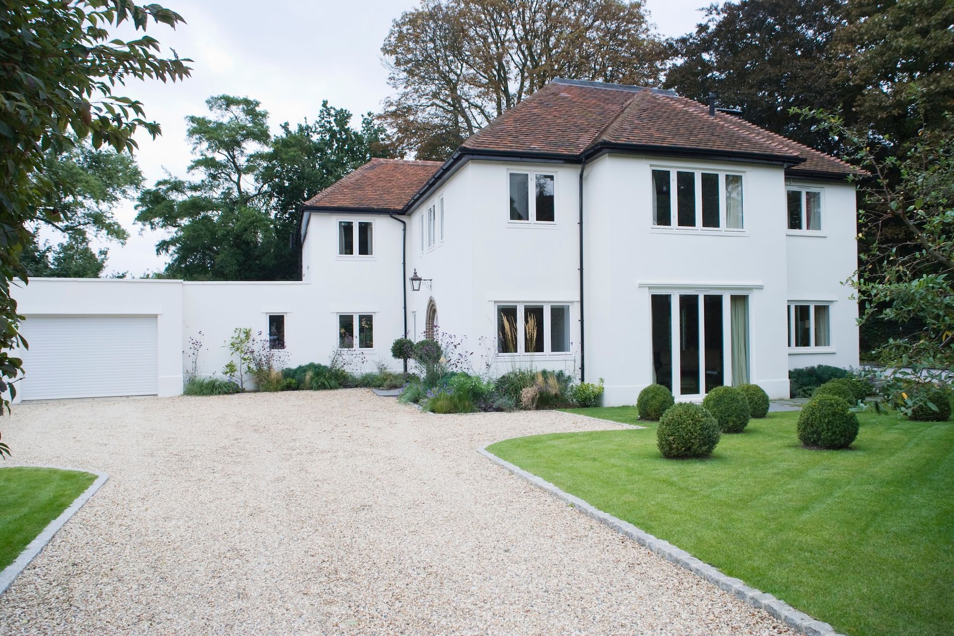 White two-story house with a gravel driveway, green lawn, and attached garage. Brown tiled roof.
