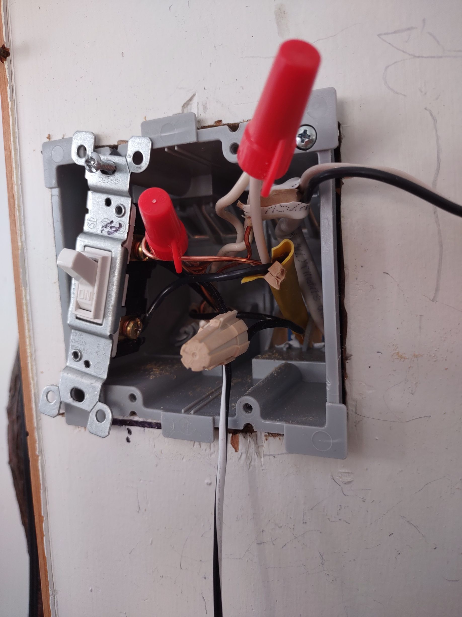 Open electrical box with wires, switch, and red safety caps.