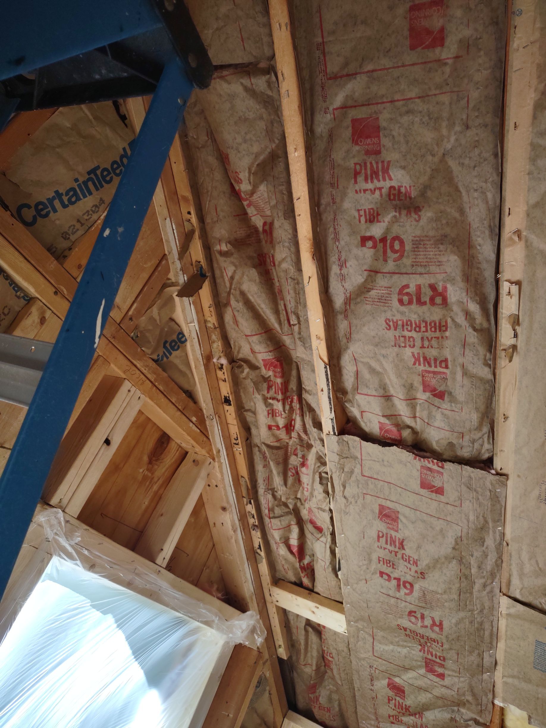 Insulation installed in an attic's angled walls, pink fiberglass in place between wooden beams.