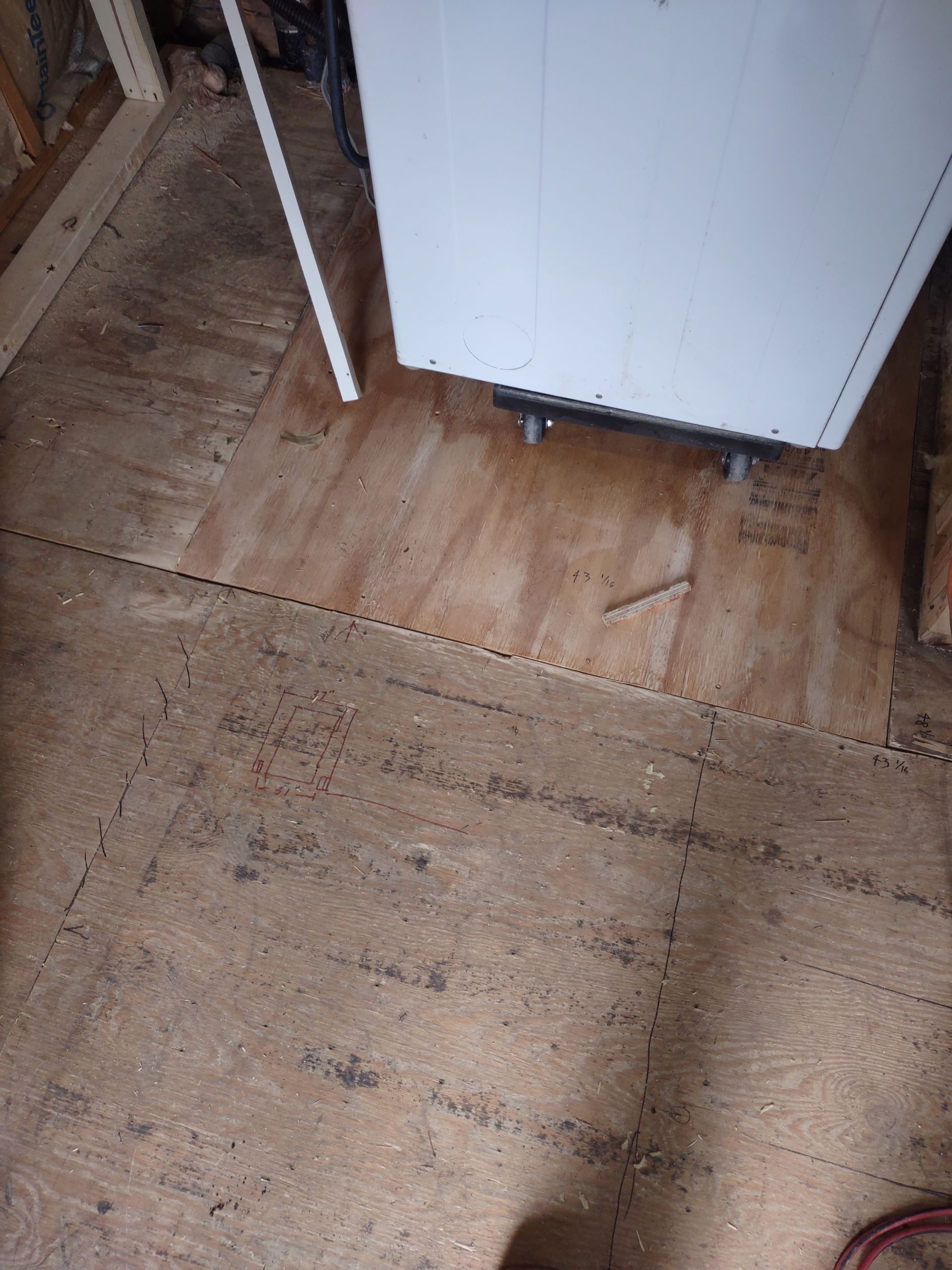 Plywood floor in room; white appliance with dark base. Floor is dusty with a seam running across.