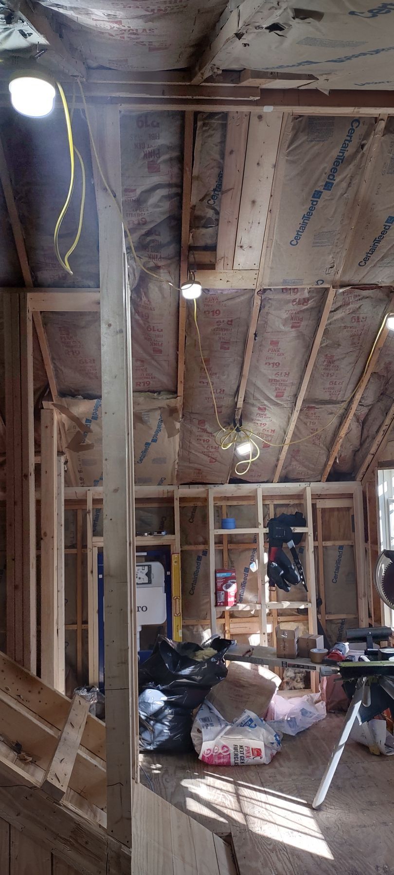 Interior of a building under construction. Studs and insulation are visible.  Materials and trash are in the foreground.