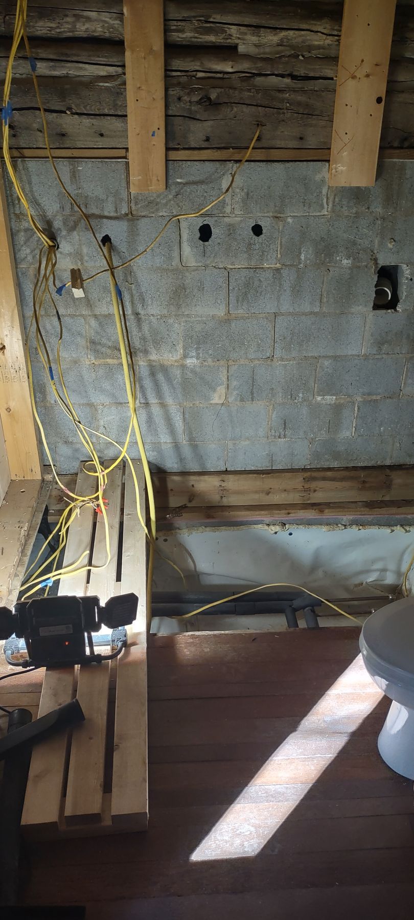 Interior construction site: concrete block wall with electrical wiring and exposed wooden beams.