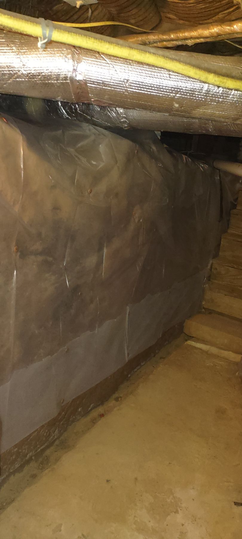 A crawl space with plastic sheeting covering the walls, and insulation above. Yellow wire is visible.