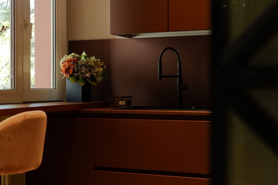 A modern kitchen with dark orange cabinets, a black faucet, and a vase of flowers on the counter.