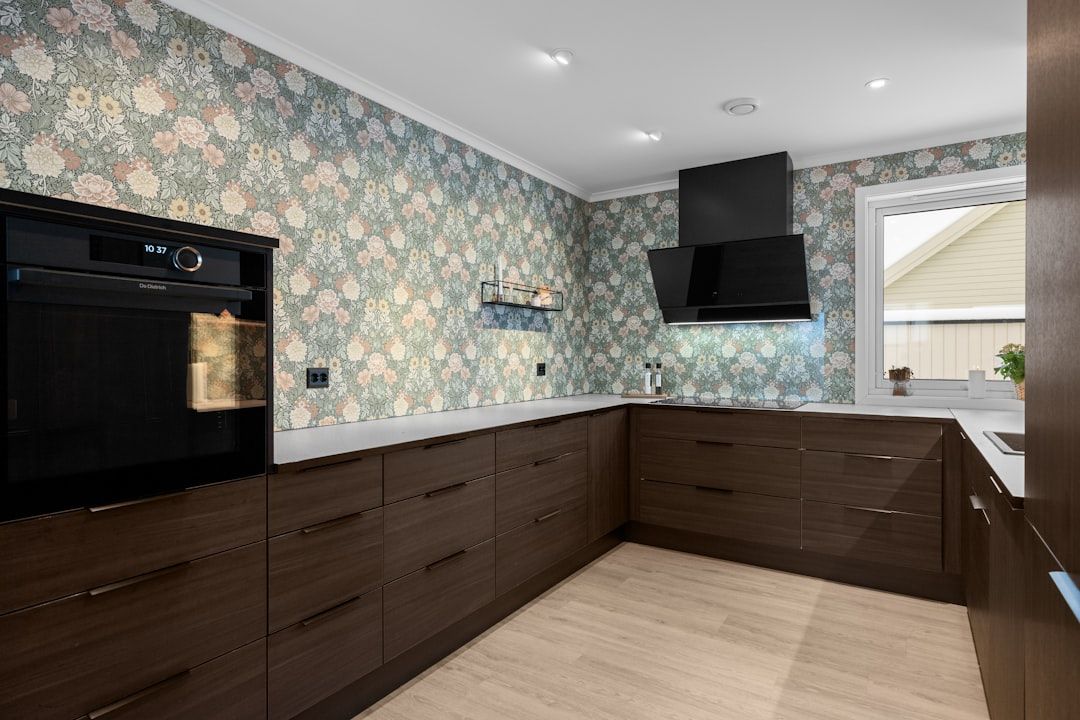 Dark wood kitchen cabinets and appliances with floral wallpaper. A window reveals an exterior view.
