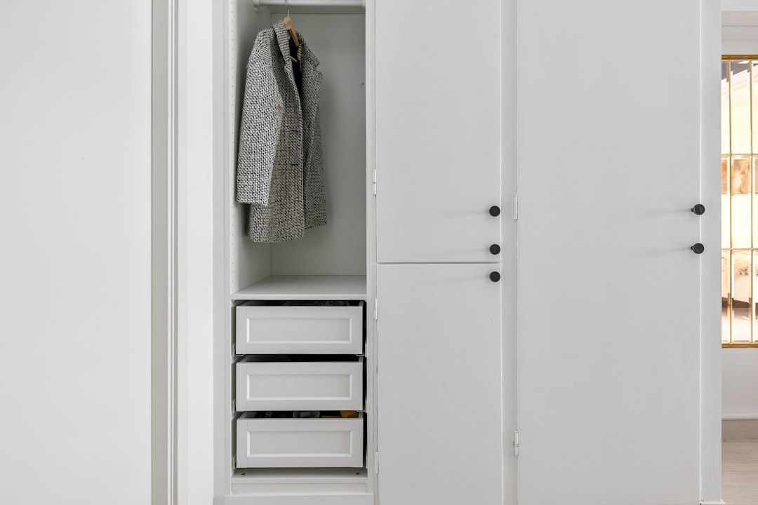 White closet with open section displaying a coat and drawers; closed sections with black knobs.