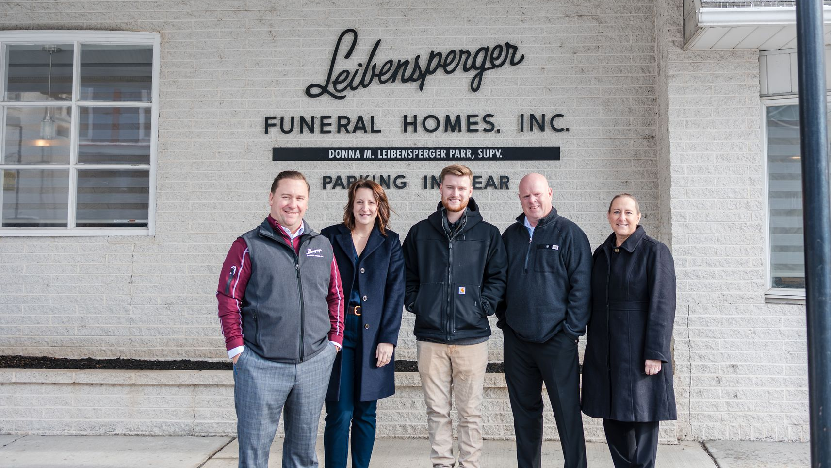 Five people stand in front of Leber Funeral Homes. A brick building and the parking sign are visible.