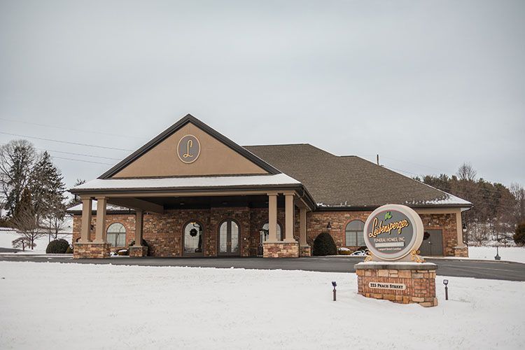 Funeral home with brick facade and sign, snow-covered ground, overcast sky.