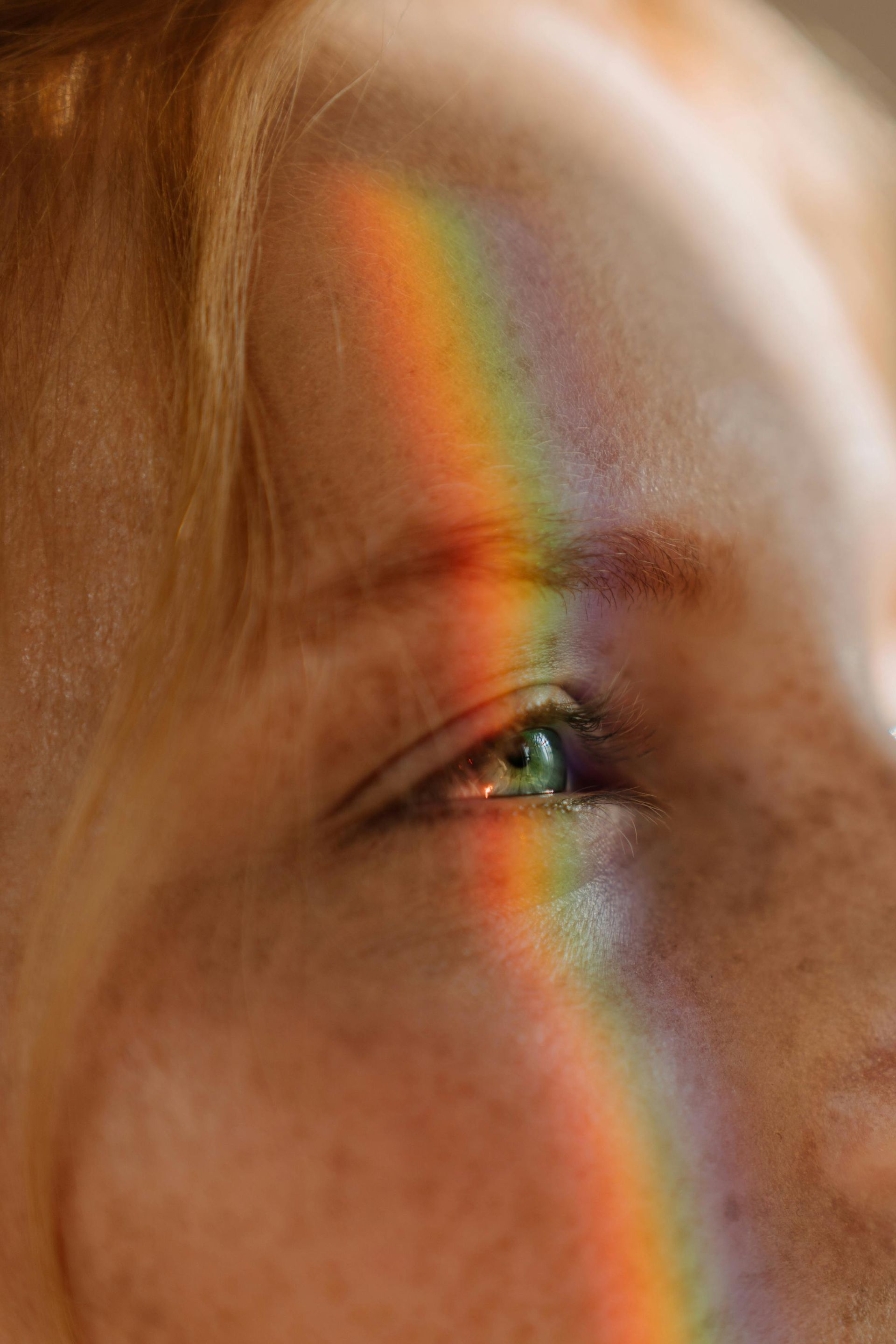A close-up shot of a rainbow shining in a person's light green eye.