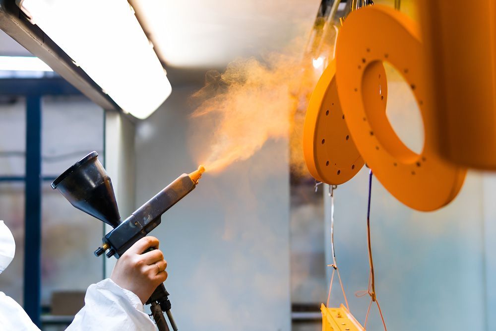 A Man in a Protective Suit is Spraying an Orange Paint on a Wall — Mudgee Powder Coat Pty Ltd in Mudgee, NSW