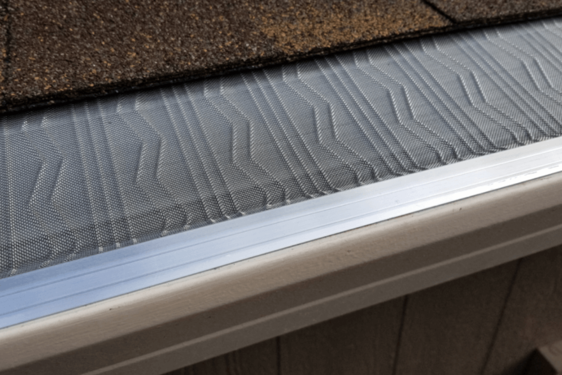A close up of a gutter with a roof in the background.