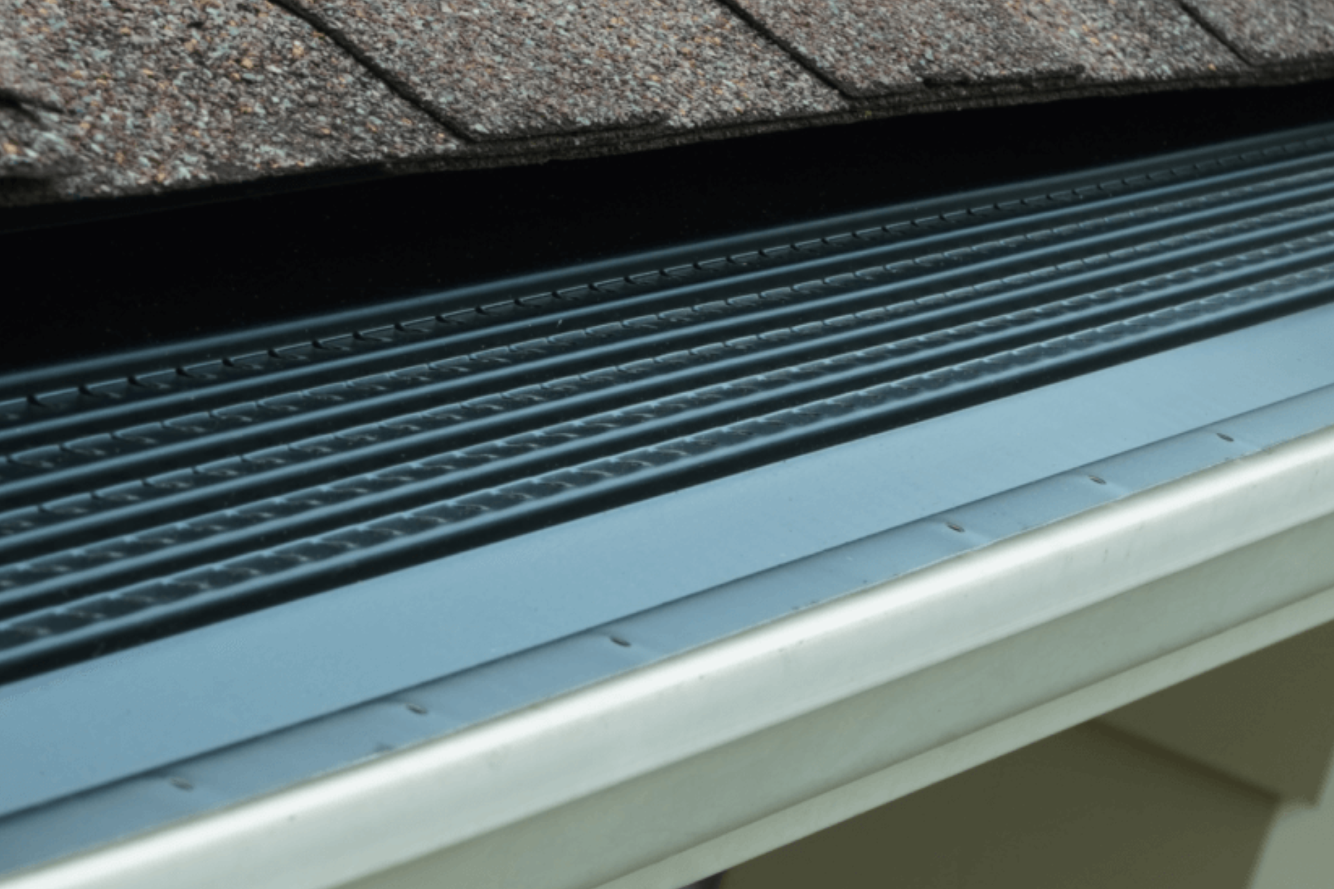 A close up of a gutter with a roof in the background.