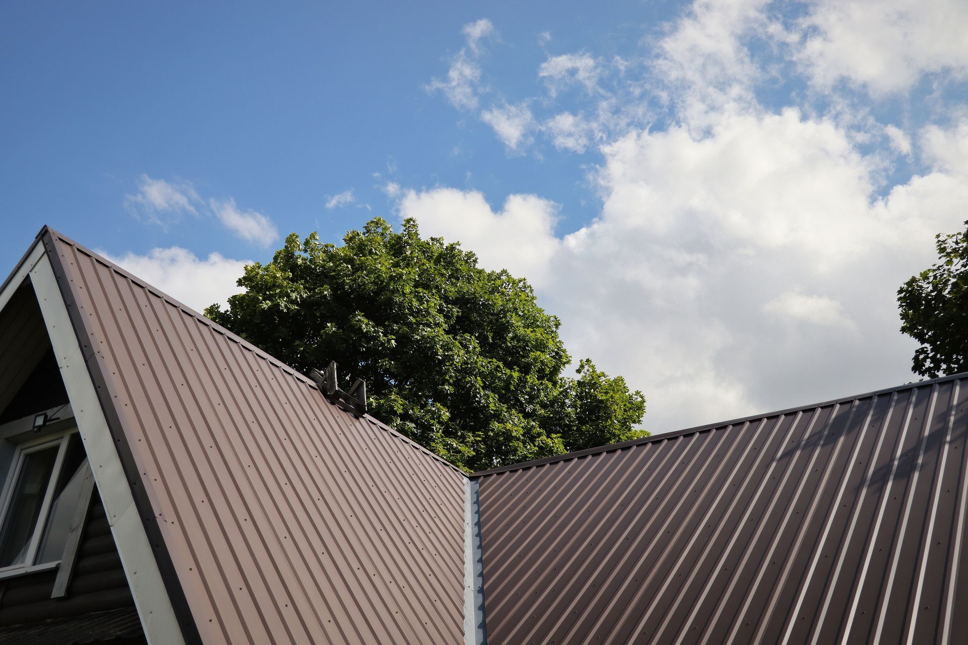 A brown roof with a tree in the background and a blue sky with clouds
