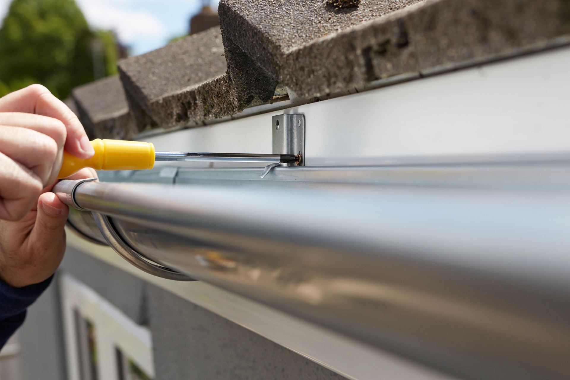 A person is fixing a gutter with a screwdriver.