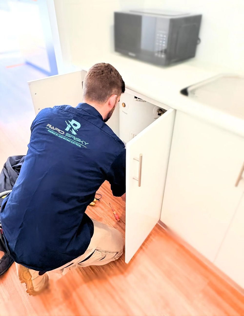 An Electrician Working on the Cabinet Under a Microwave — Rapid Sparky in Wollongong, NSW