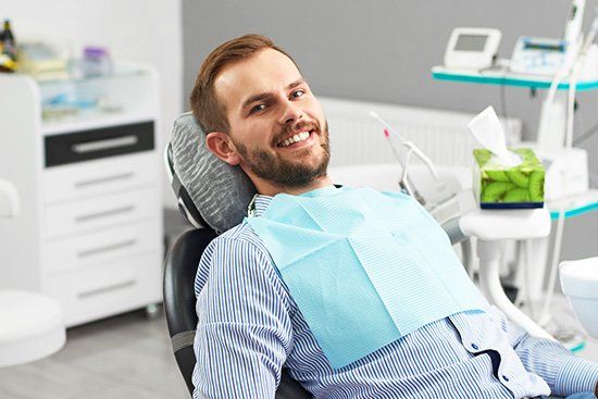 Man smiling in a dentist chair wearing a blue bib; dental office in background.