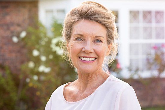 Smiling older woman with light hair in front of a brick house.