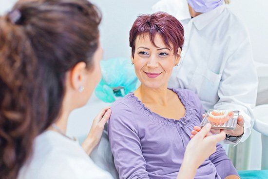 Woman at dentist smiles as dental professional holds a model of teeth.