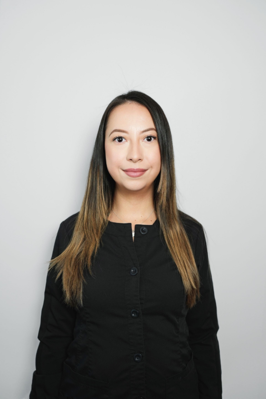 Woman with long brown hair, wearing a black button-up shirt, smiling in front of a gray background.
