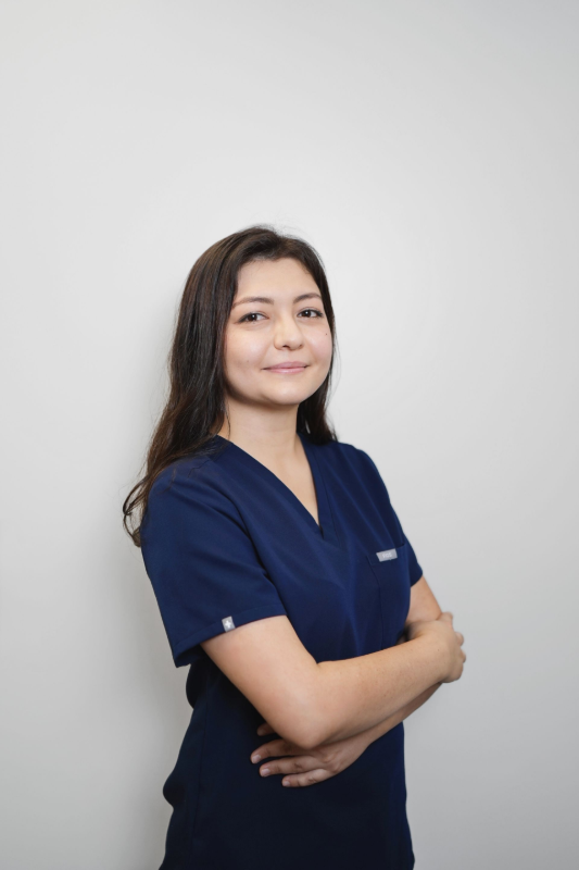 Woman in navy scrubs with arms crossed, smiling against a light gray background.