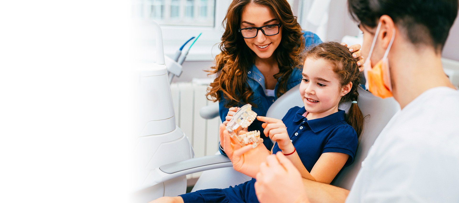 Dentist showing a child a teeth model with the mother present. Smiling faces.