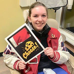 Woman in dental chair smiles, holding 