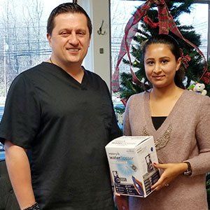 Man in black scrubs and woman holding a water filter, smiling near a Christmas tree.