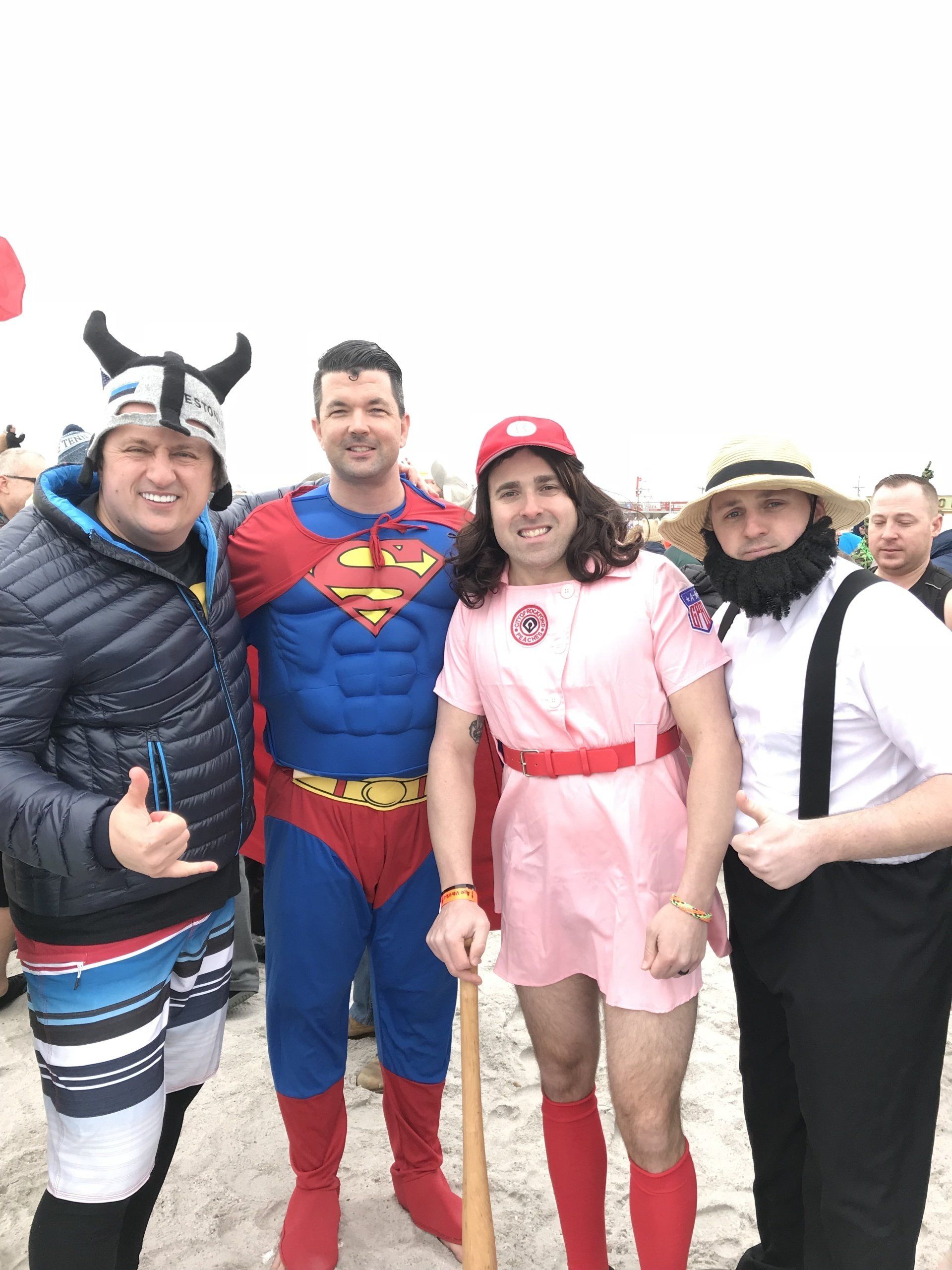 Four people in costumes pose outside. One is Superman, one is a baseball player, one is an Amish person, and one is a Viking.