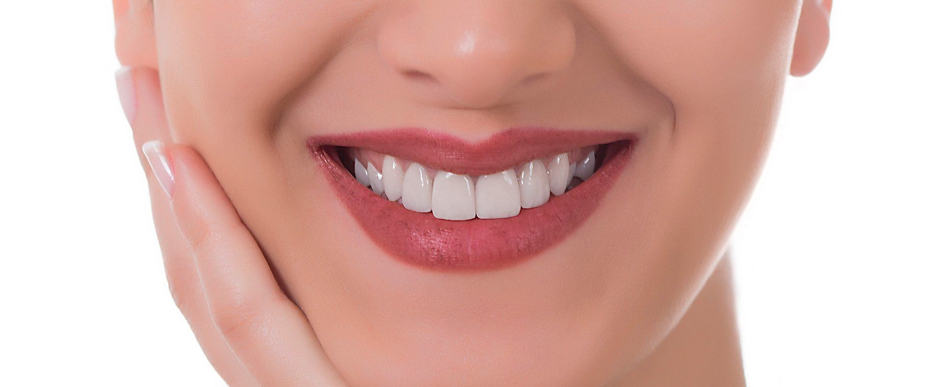 Close-up of a smiling person with white teeth and red lipstick, hand on cheek.