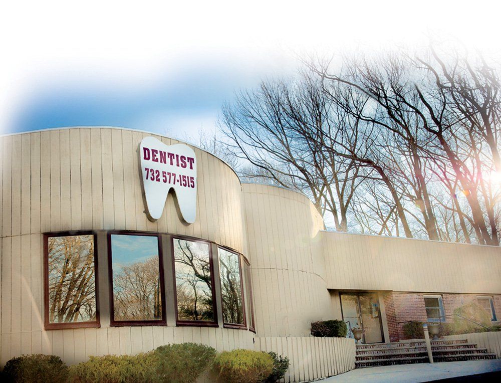 Dentist office with a tooth sign, brown building, windows, trees in the background, blue sky.